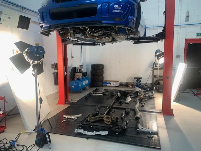 A blue car is on a lift in a garage.
